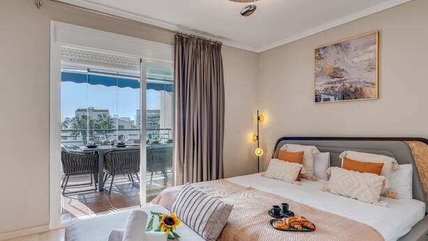 A hotel room with a bed, a balcony with a table and chairs, and a painting on the wall.