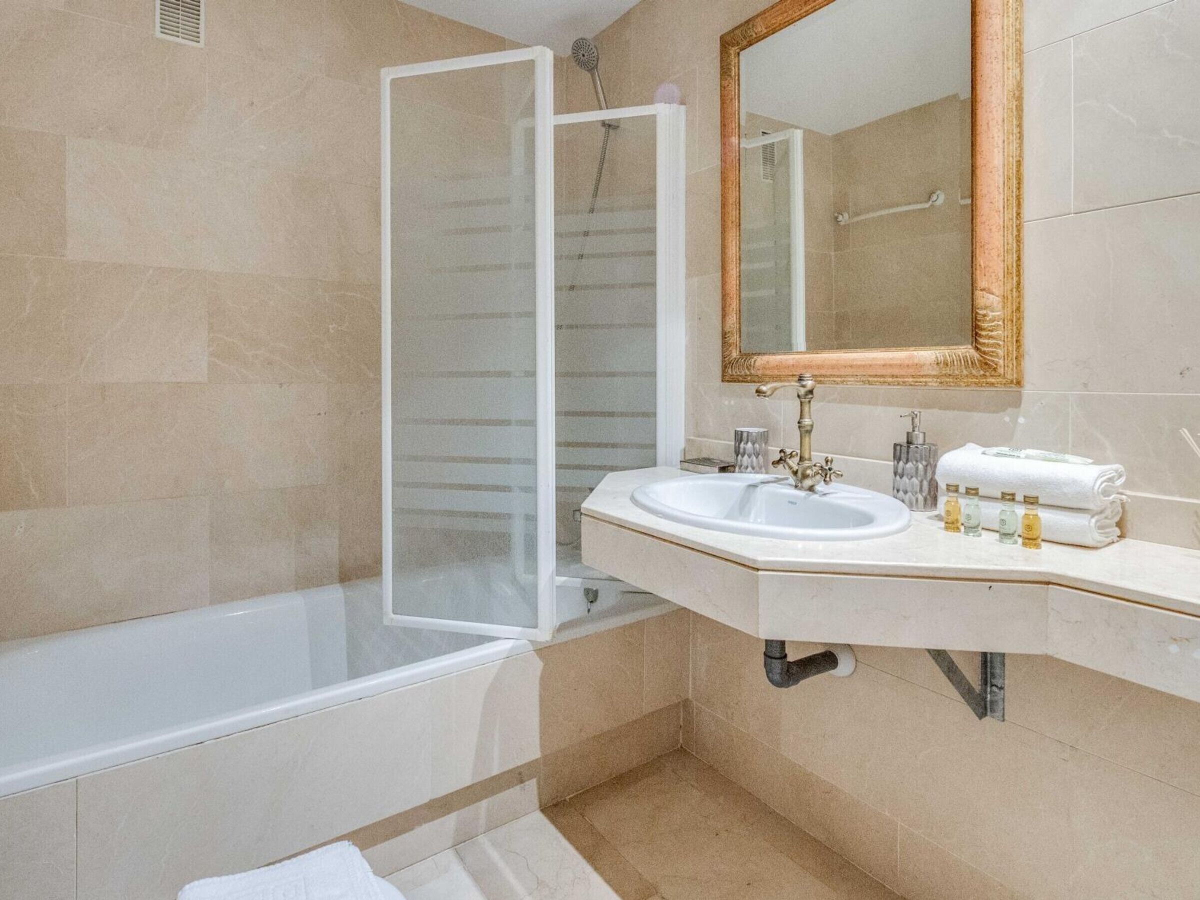 Un baño con bañera, cabina de ducha, lavabo con espejo y artículos de aseo.