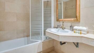 Un baño con bañera, cabina de ducha, lavabo con espejo y artículos de aseo.