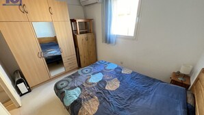 A bedroom with a bed, a wardrobe, a small table, and an air conditioning unit.