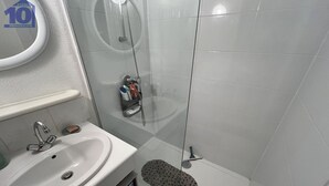 A bathroom with a sink, mirror, shower, and a small shelf with toiletries.