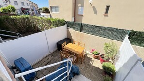 A small patio area with a wooden table and chairs, a barbecue grill, and potted plants.