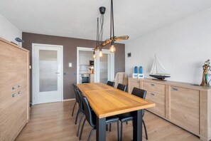 A modern kitchen with a wooden table and chairs, a hanging light fixture, and a cabinet with a sailboat model.
