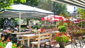 Ein Straßencafé mit Holztischen und -bänken, umgeben von Blumentöpfen und Blumen.