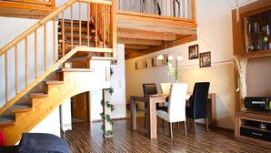 Ein modernes Interieur mit einer Holztreppe, einer Essecke mit Tisch und Stühlen sowie einem Wohnbereich mit Fernseher und Zimmerpflanzen.
