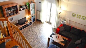 Ein Wohnzimmer mit einer Holztreppe, einem Sofa, einem Fernseher und einem Bücherregal.