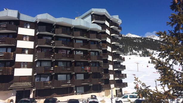 A multi-story hotel with balconies and a ski slope in the background.
