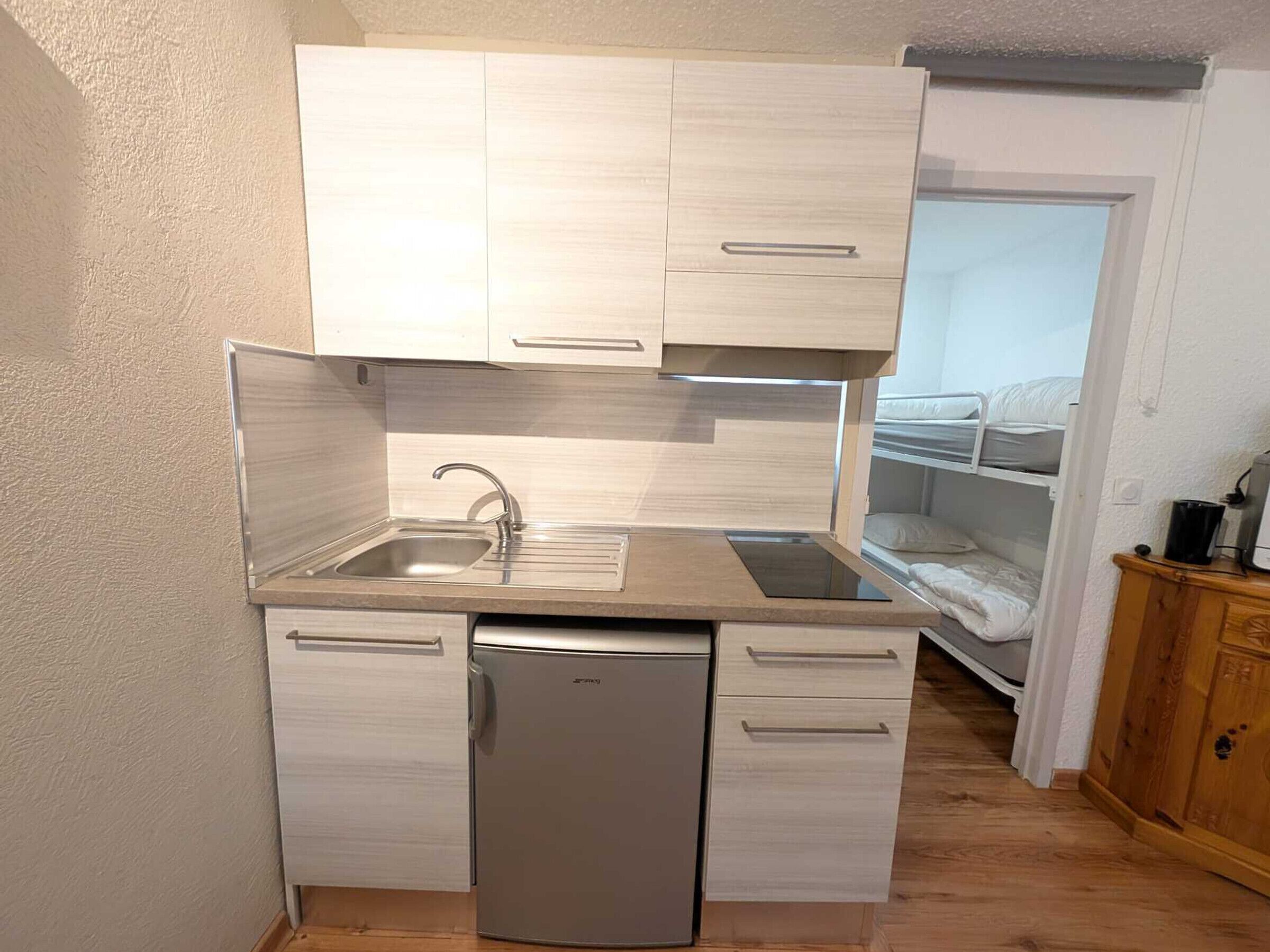 Eine kompakte Küchenzeile mit integriertem Geschirrspüler, Spüle und kleinem Kühlschrank.