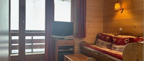 A cozy room with a wooden interior, a sofa with patterned cushions, a television on a wooden stand, and a window with curtains.