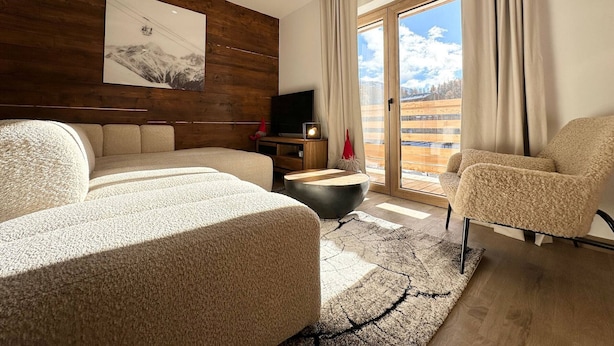 Un soggiorno moderno con una parete d'accento in legno, un'ampia finestra vista su un paesaggio innevato, un divano, una poltrona e un televisore a schermo piatto.