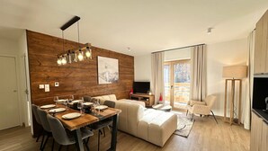 Un soggiorno moderno con una parete d'accento in legno, un'area pranzo con tavolo e sedie in legno, un divano e una televisione.