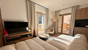 Una camera d'albergo moderna con un ampio divano, una TV a schermo piatto, un tavolino e una poltrona.