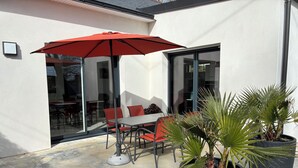 Une terrasse avec une table et des chaises, un parasol rouge et des plantes en pot.