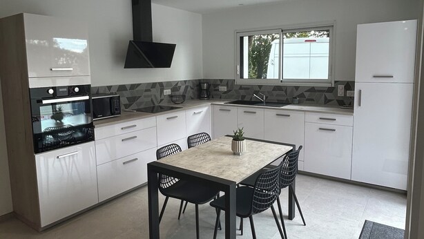Une cuisine moderne avec des meubles blancs, une cuisinière noire et un coin repas comprenant une table et des chaises.