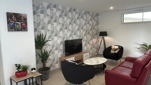 Un salon moderne avec un téléviseur à écran plat, un canapé rouge, un fauteuil noir, une petite table basse et un mur orné d’un motif.