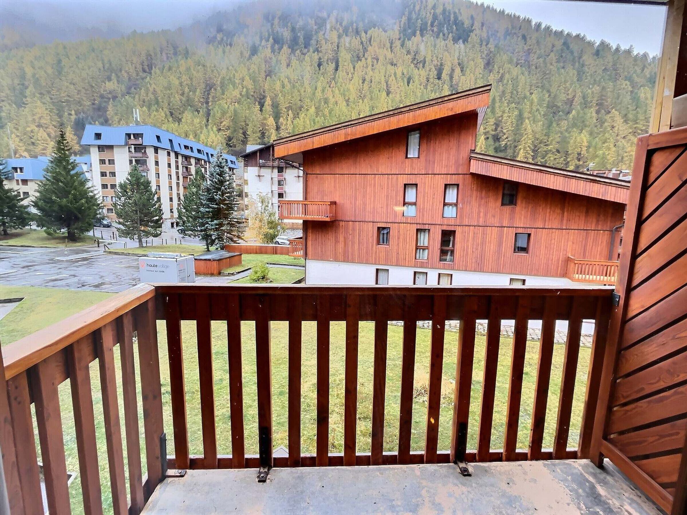 A wooden balcony with a view of a mountain and a building with multiple windows.