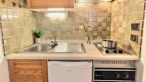 Een kleine keuken met een spoelbak, fornuis en een kleine koelkast.