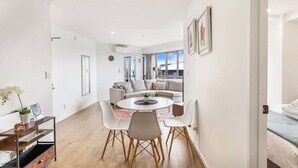 A modern living room with a round dining table, white chairs, a sofa, and a large window with a view.