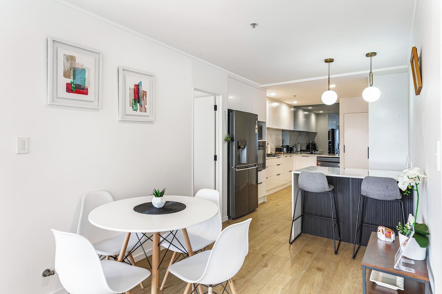 A modern kitchen with white cabinetry, a built-in oven, and a dining area with a round table and white chairs.