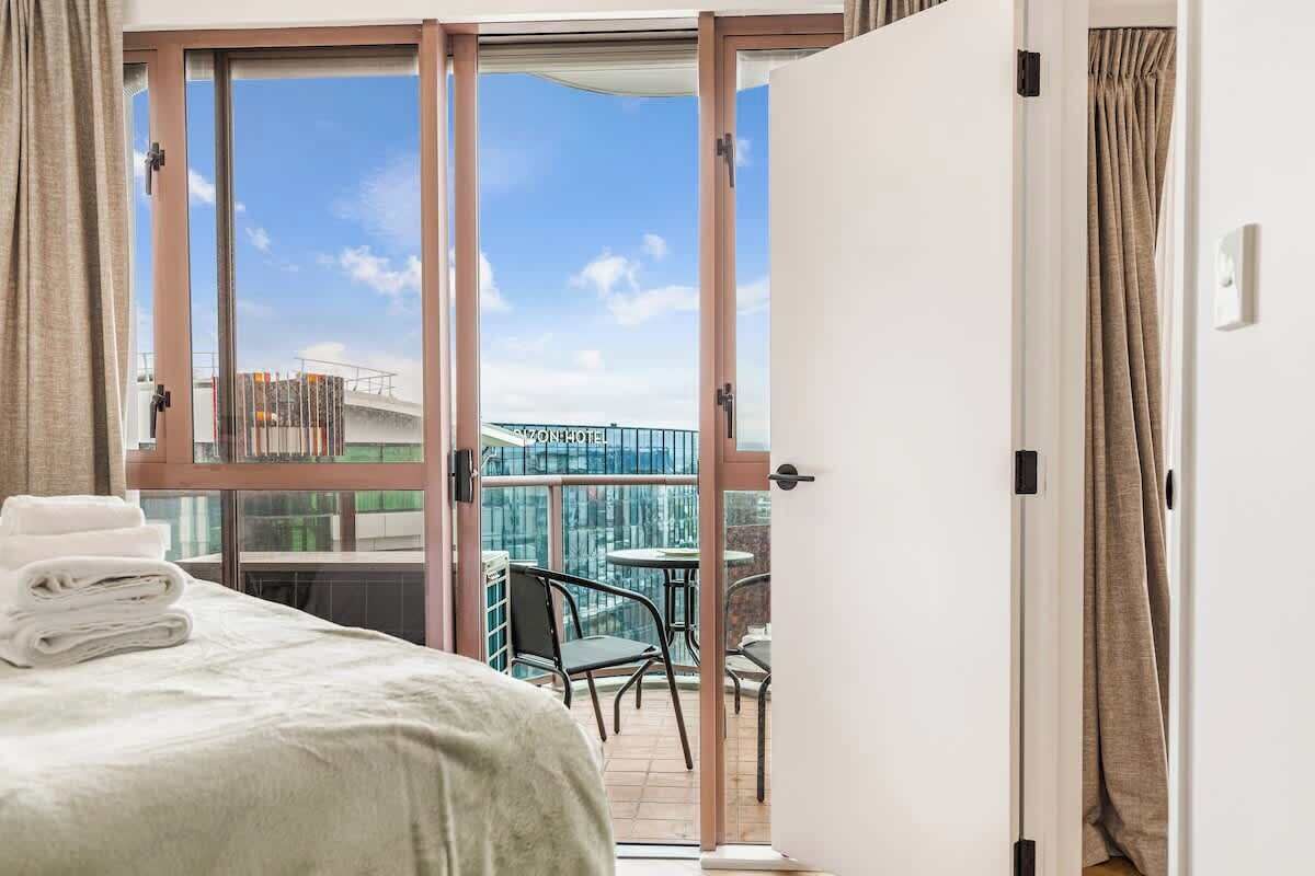 Une chambre d’hôtel avec un lit, un balcon donnant sur un pont et un immeuble, ainsi qu’une table et des chaises à l’extérieur.