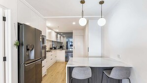 A modern kitchen with a large refrigerator, a marble island, and two bar stools.