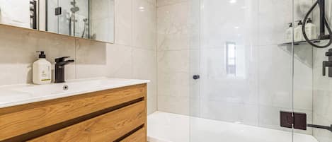 A modern bathroom with a glass-enclosed shower, a wooden vanity with a white countertop, and a large mirror above the vanity.