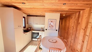 Een kleine keuken met witte kastjes, een eettafel met stoelen en een houten plafond.