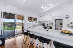 A modern kitchen with a large island, bar stools, a refrigerator, and a view of the outdoors.