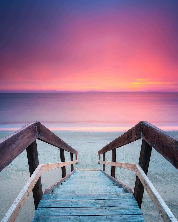 A wooden boardwalk leading to a beach with a sunset in the background.