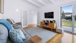 En moderne stue med sofa, sofabord, fjernsyn og en skydedør til haven.