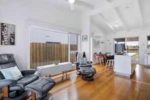 A modern living room with a sofa, a chair, a dining area, and a kitchen with a view.