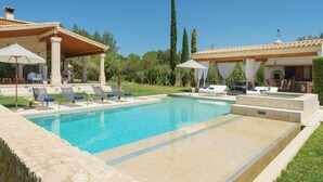 Una piscina con sillones de descanso y sombrillas, rodeada por un muro de piedra y vegetación.