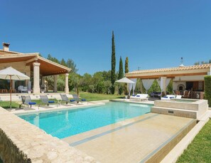 A swimming pool with lounge chairs and umbrellas, surrounded by a stone wall and greenery.
