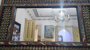 A room with a large ornate mirror, a chandelier, and framed artwork on the walls. - blue city (Chefchaouen)