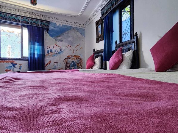 A bedroom with a large bed, a mural on the wall, and a window with blue curtains. - blue city (Chefchaouen)