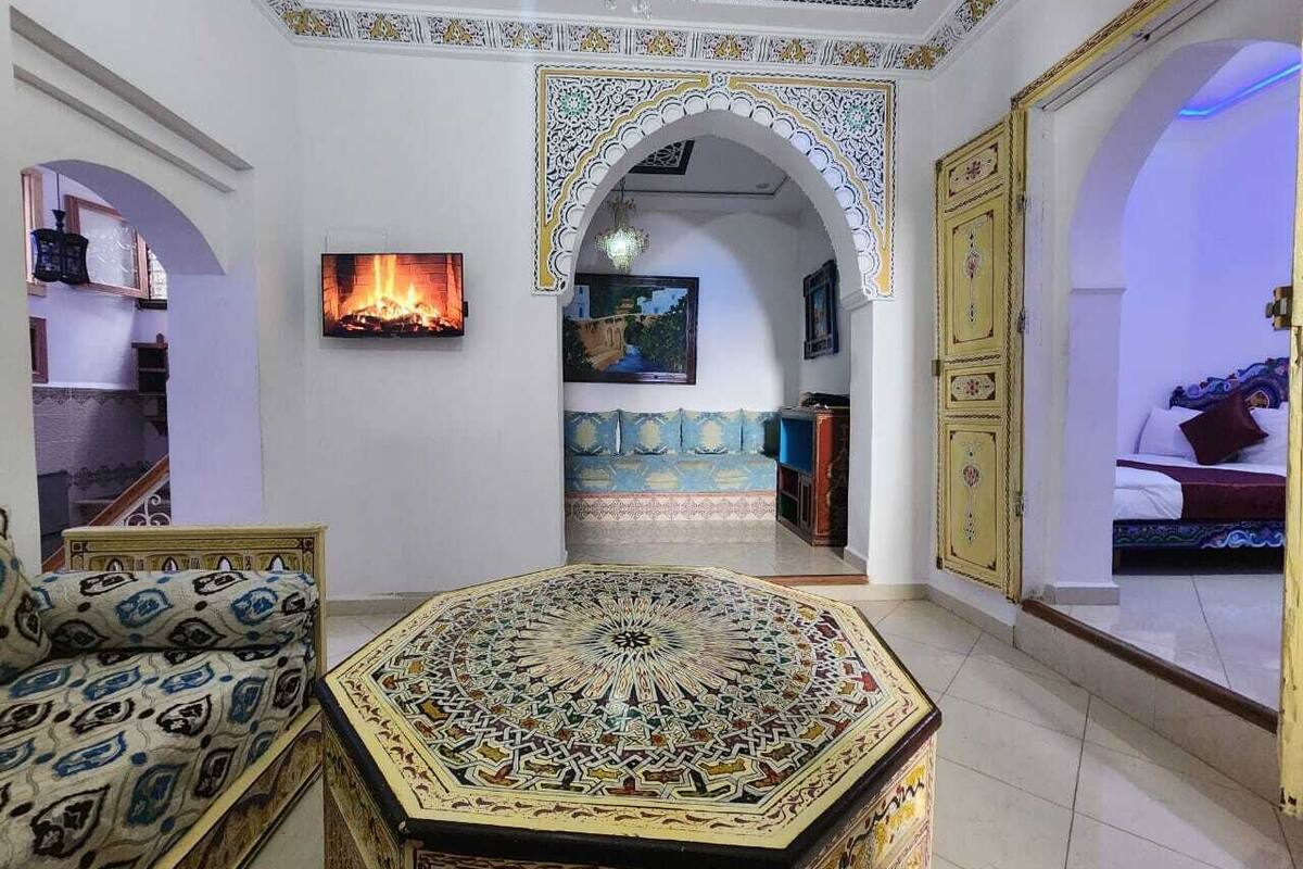 A room with a large, ornate rug, a sofa, a television, and a bed with a blue and white patterned bedspread.