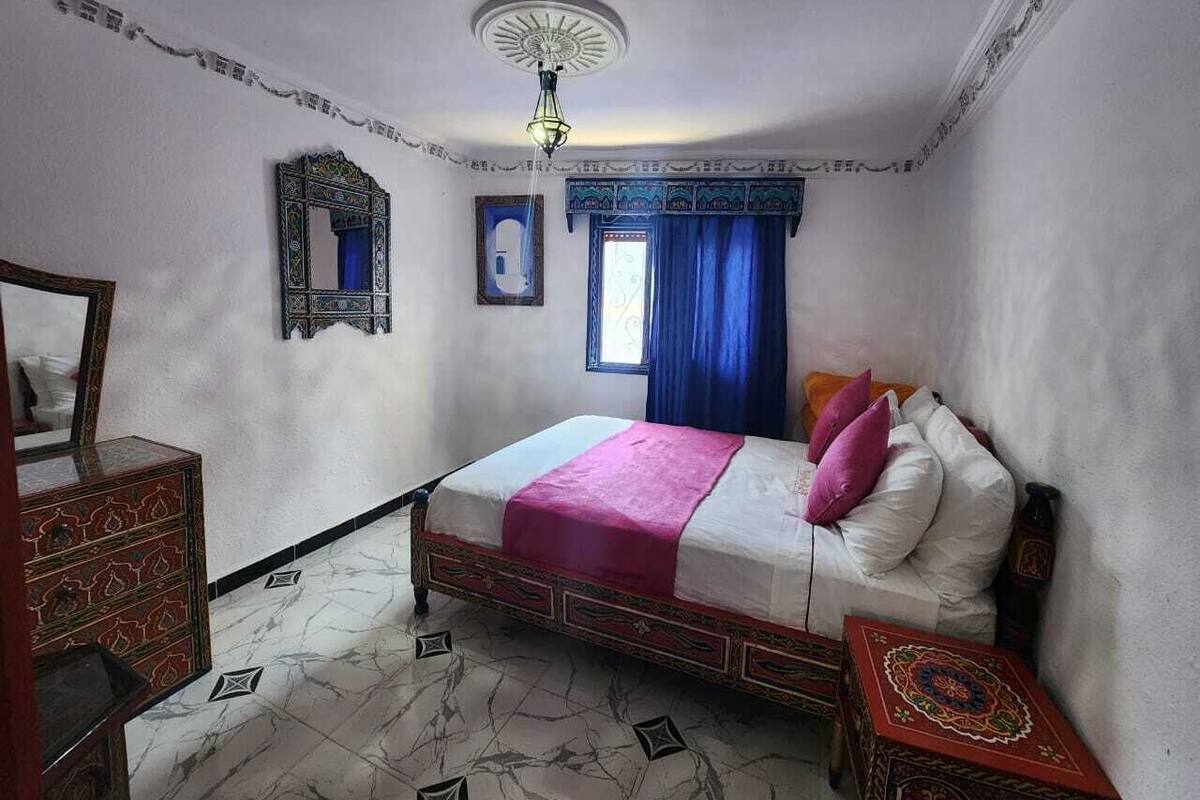 A bedroom with a bed, a dresser, a mirror, and a window with blue curtains.
