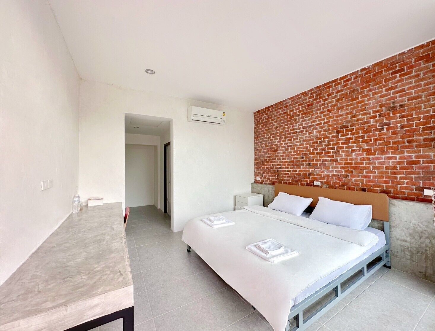 Quarto com cama, mesa de cabeceira, uma mesa e parede de tijolos.