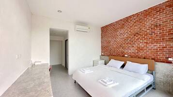 Quarto com cama, mesa de cabeceira, uma mesa e parede de tijolos.