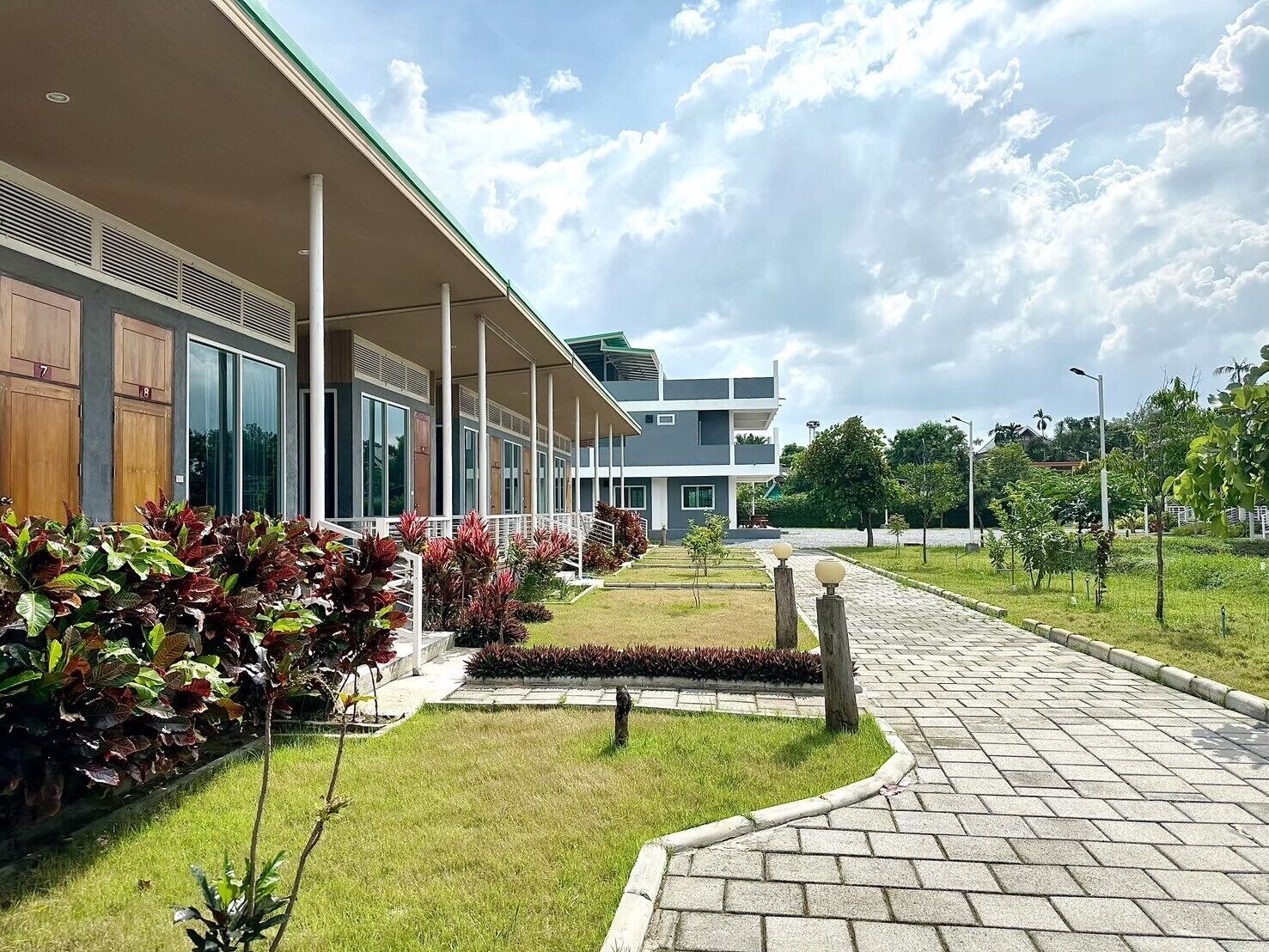 A modern building with a covered walkway, large windows, and a well-maintained garden with various plants.