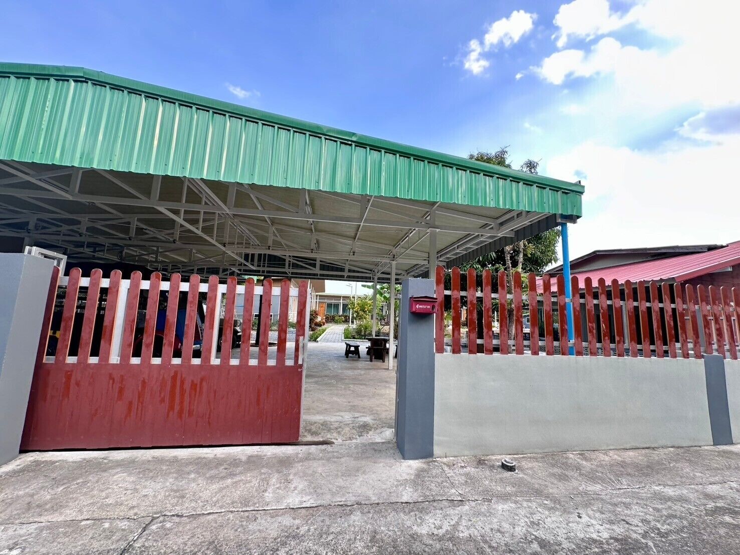 A covered outdoor area with a green roof, a red and white fence, and a mailbox.
