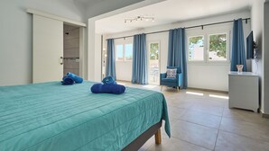 Un dormitorio amplio con una cama grande, un vestidor, un balcón con cortinas azules y vistas al exterior.
