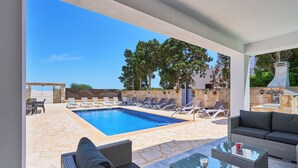 Un área junto a la piscina con sillones de descanso, un sofá y una mesa de vidrio.