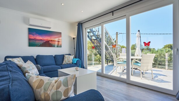Un salón moderno con un sofá azul, una mesa de centro blanca y un ventanal con vistas a un balcón.