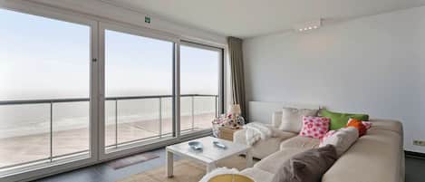 A modern living room with a large window, a sofa, a coffee table, and a lamp.