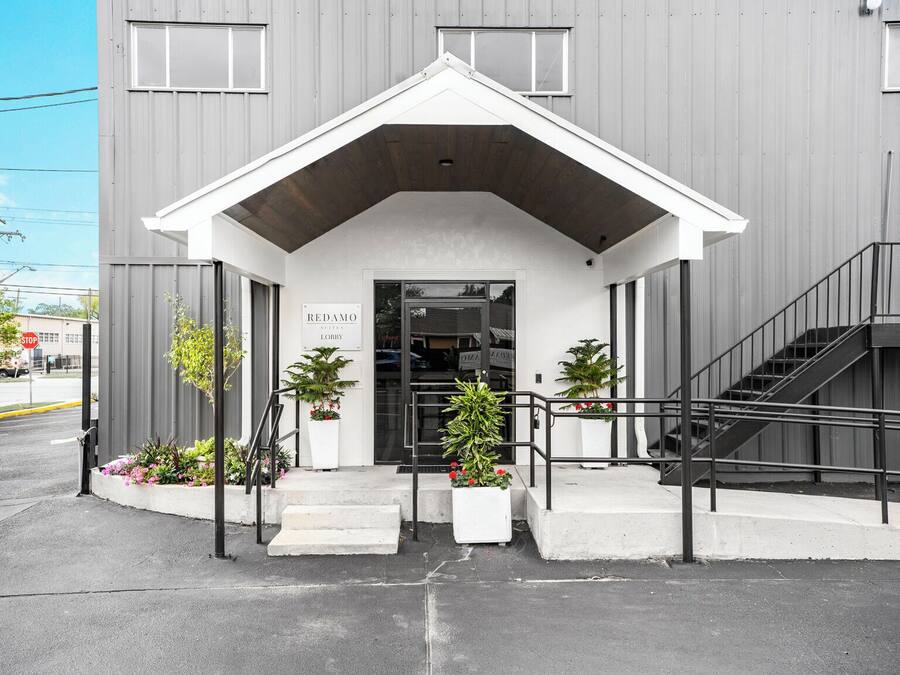 Un edificio moderno con entrada blanca, una escalera y plantas en macetas.