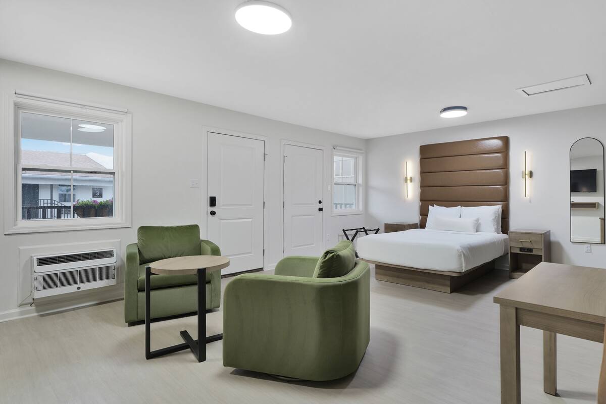 Une chambre d’hôtel avec un lit, un bureau, deux chaises, une commode et une fenêtre donnant sur un beau paysage.