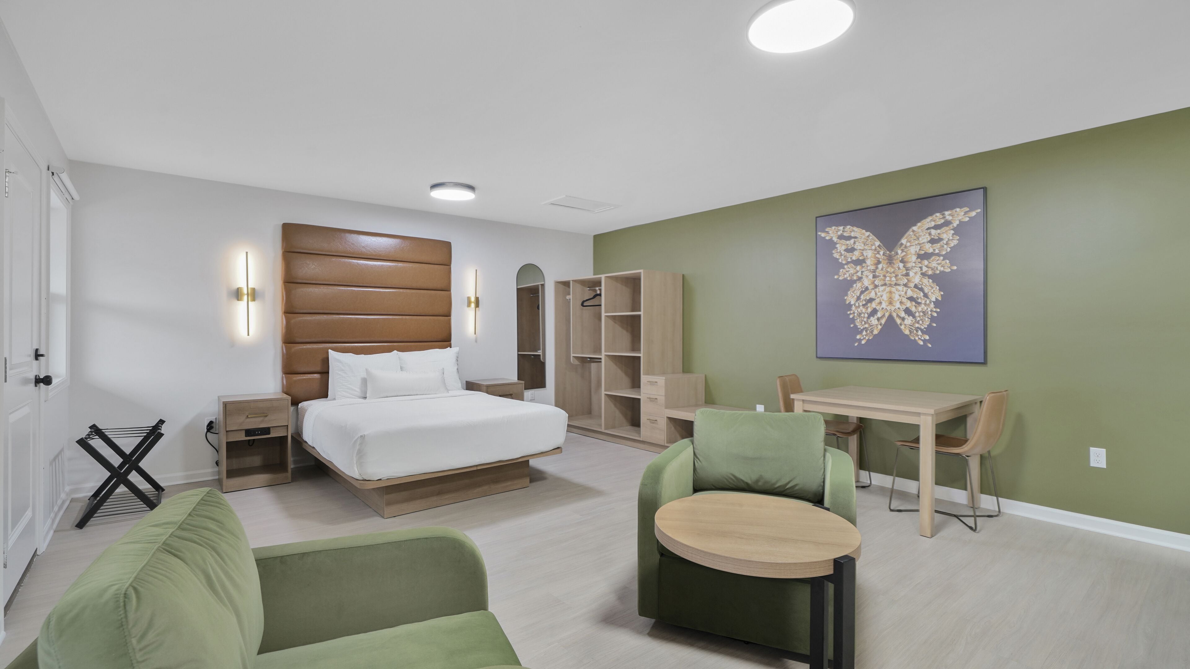Quarto moderno com cama, mesas de cabeceira, uma poltrona verde, uma mesinha redonda e um guarda-roupa.