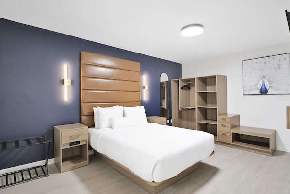 A modern bedroom with a large bed, wooden headboard, bedside tables, a wardrobe, and a hanging coat rack. - Redamo Suites (New Orleans)