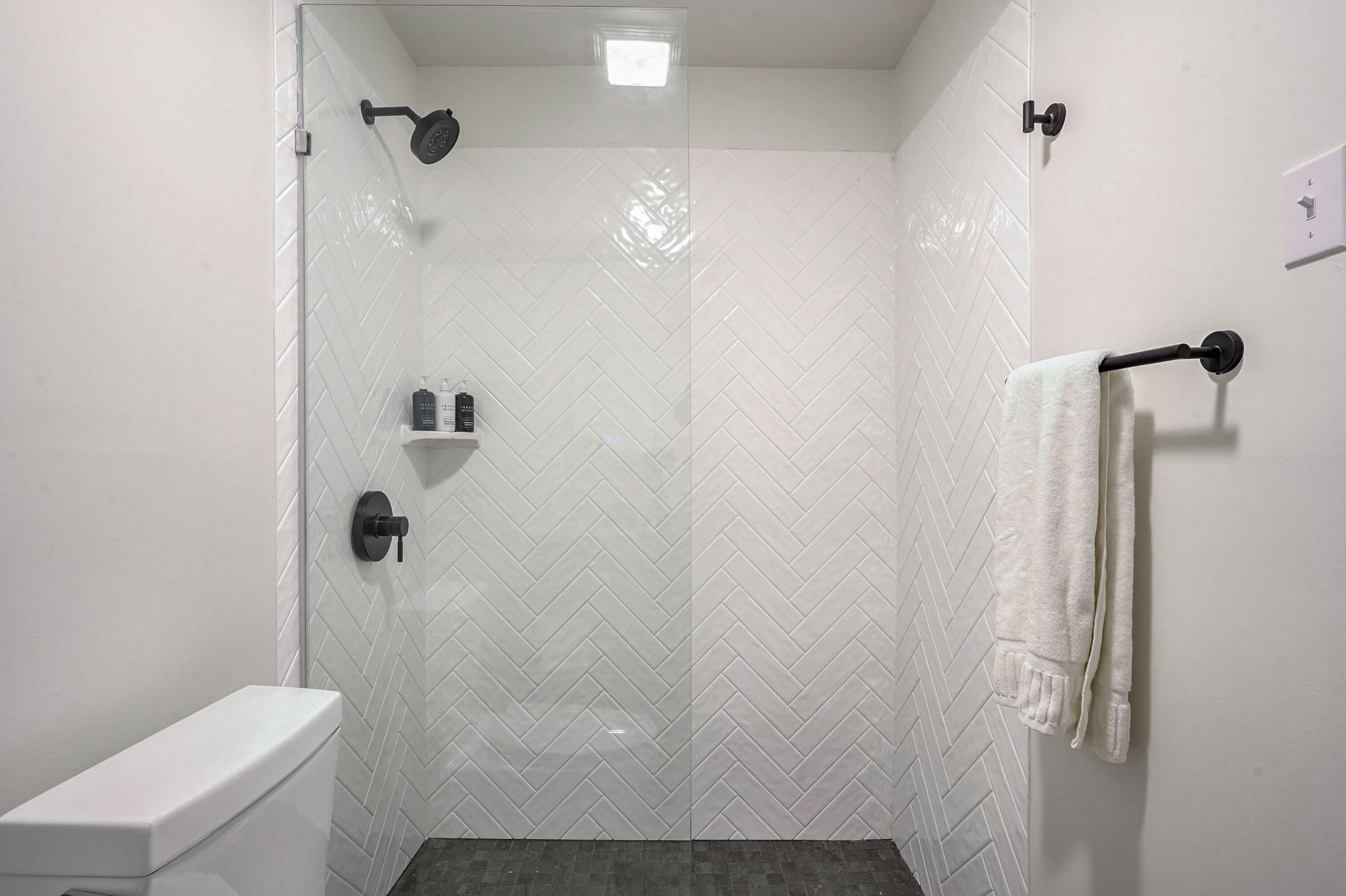 A modern shower with a glass door, a white tiled wall, and a towel rack.